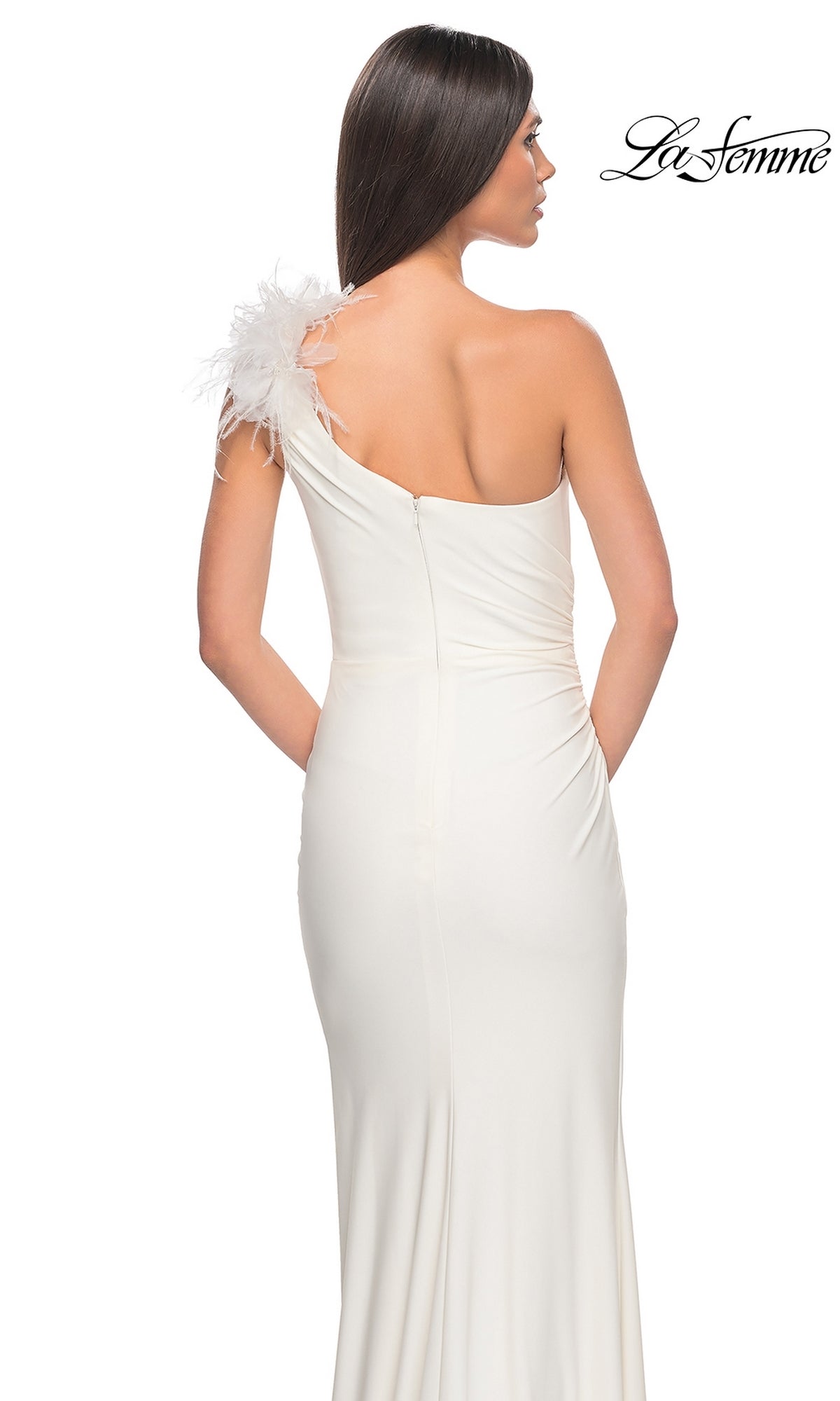 A woman stands with her back to the camera wearing the La Femme Feathered One-Shoulder Prom Dress 32076, a long, fitted white gown featuring feather detail on the shoulder.